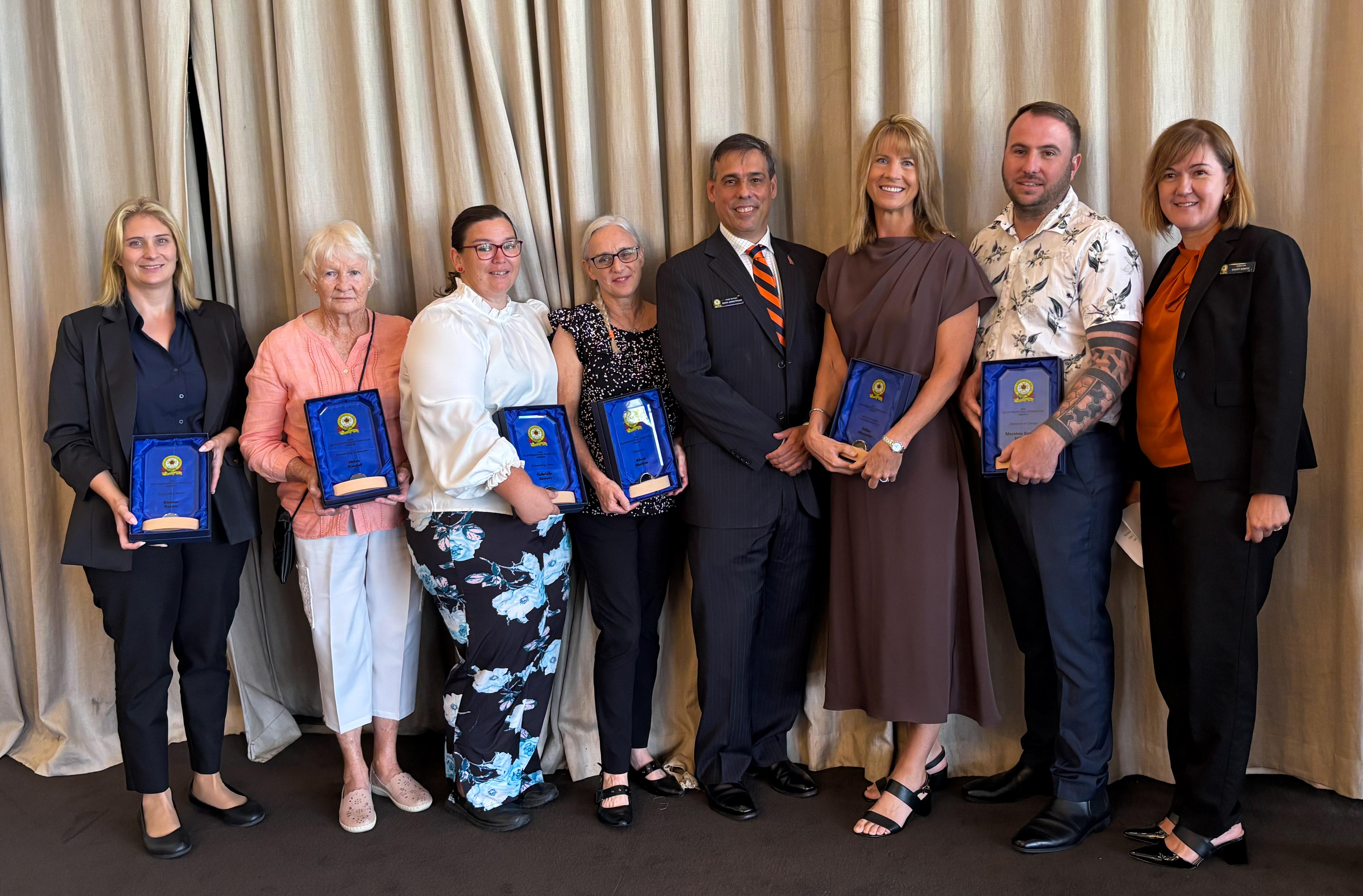 Award receivers standing in a line in front of a curtain holding awards.