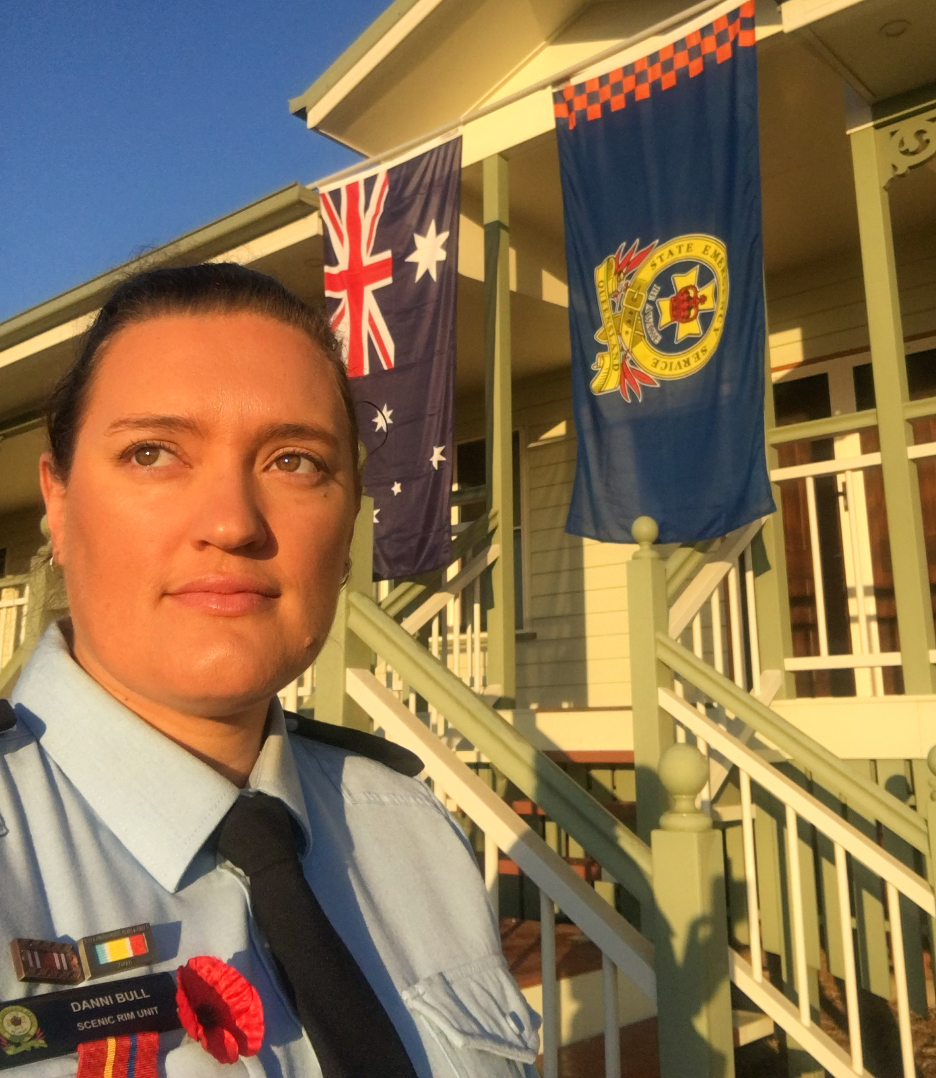 Portrait of female SES member. Standing in front of building with flags.