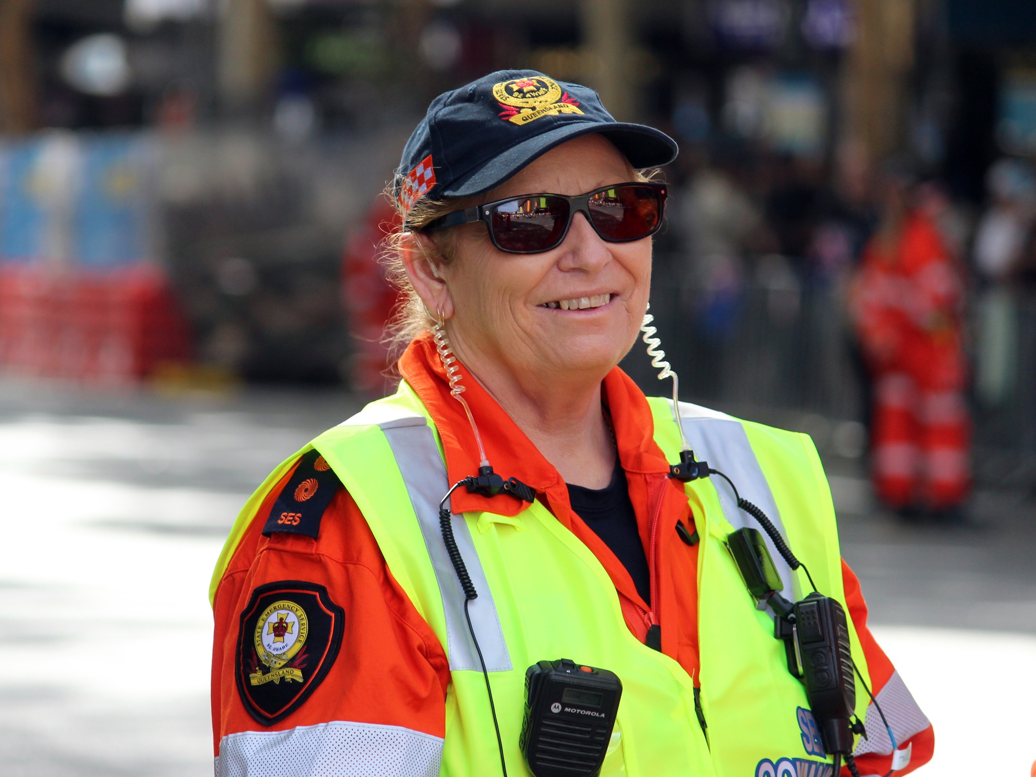 Portrait of female SES member in uniform, wearing sunglasses, cap and high visibility vest.
