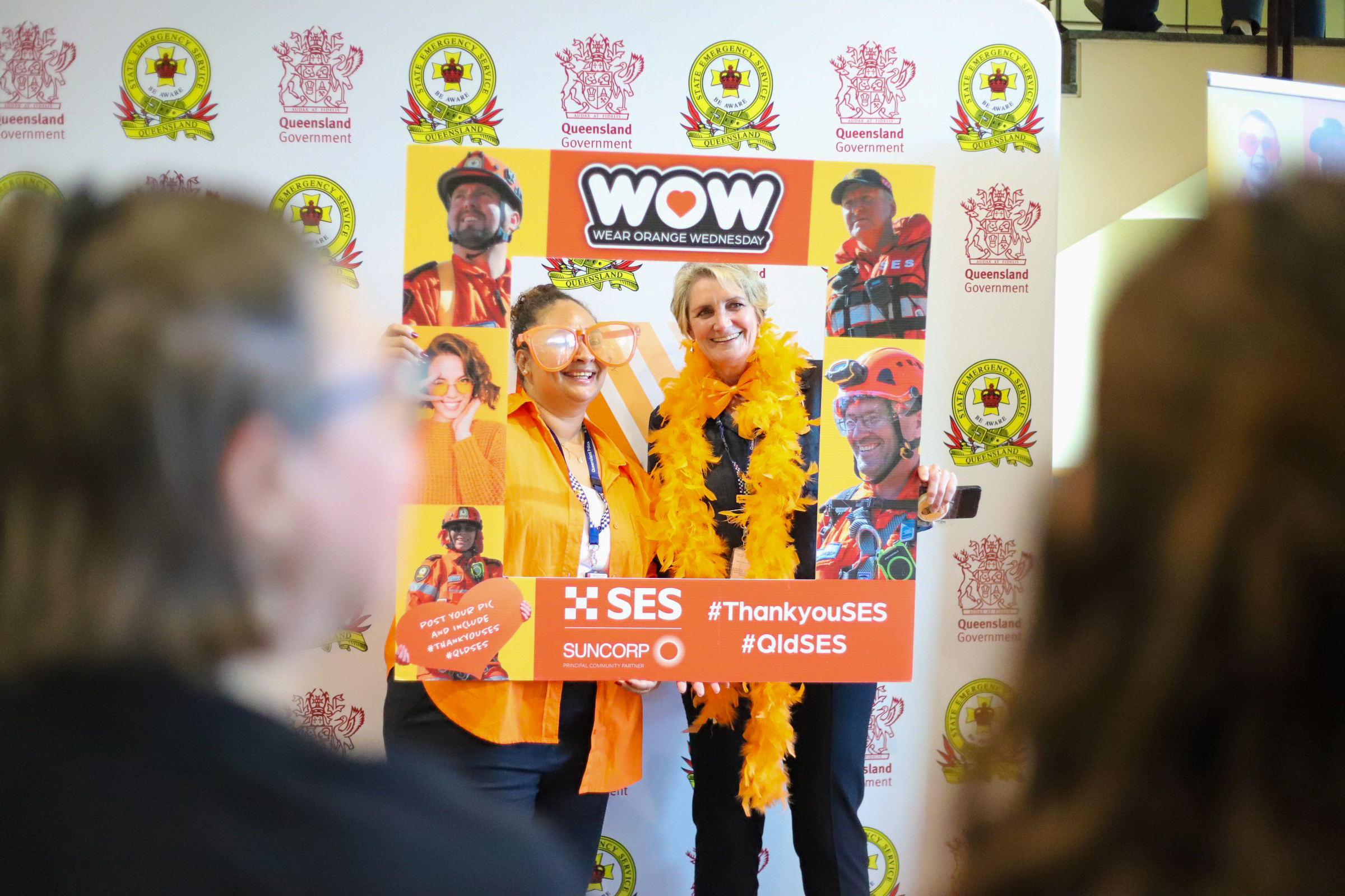 Two people hold a selfie frame posing for a photo, wearing orange accessories.