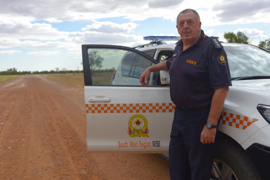 SES member John standing with SES vehicle in outback landscape.