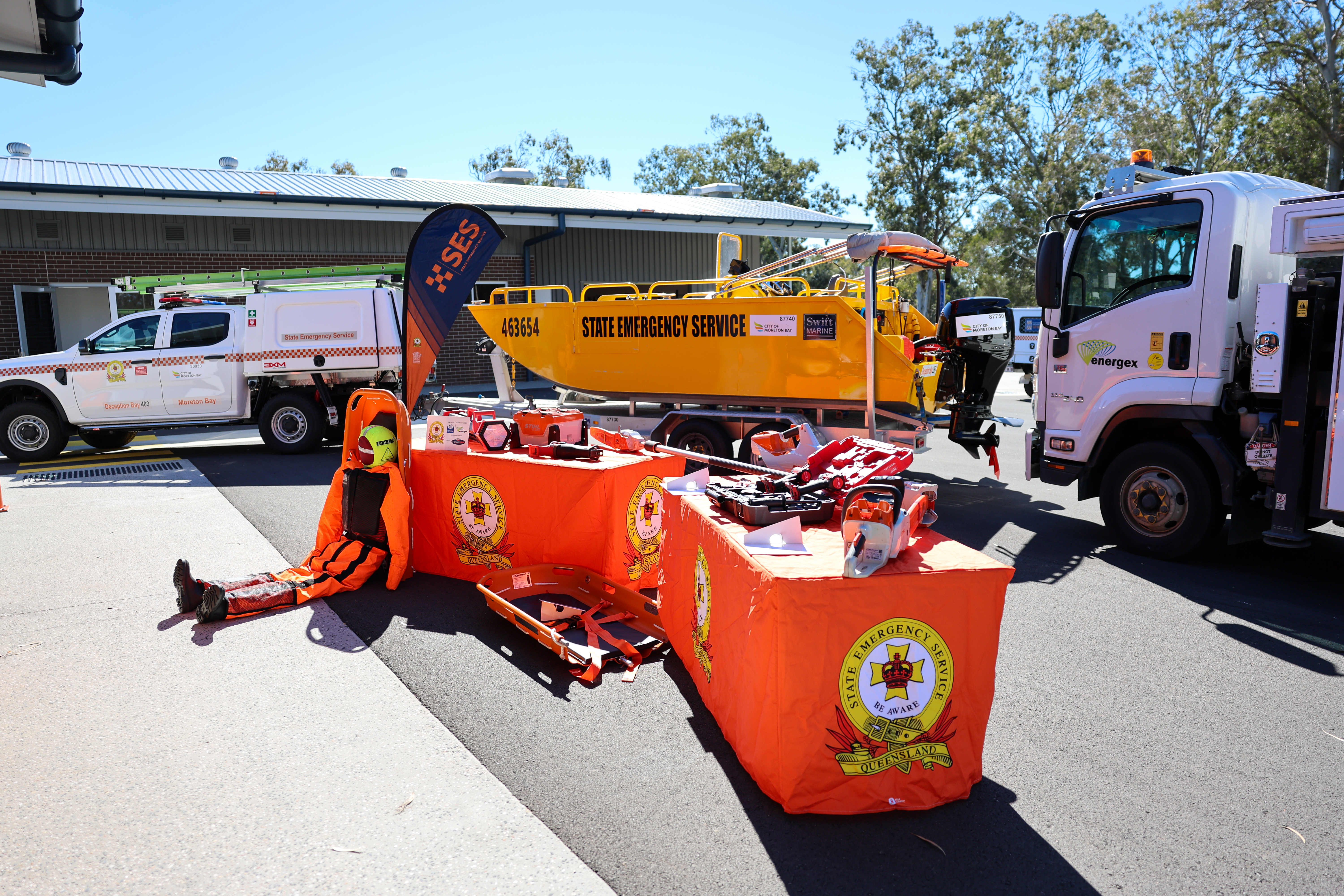 SES emergency equipment on display on SES tables with SES and energy vehicles outside of SES depot.
