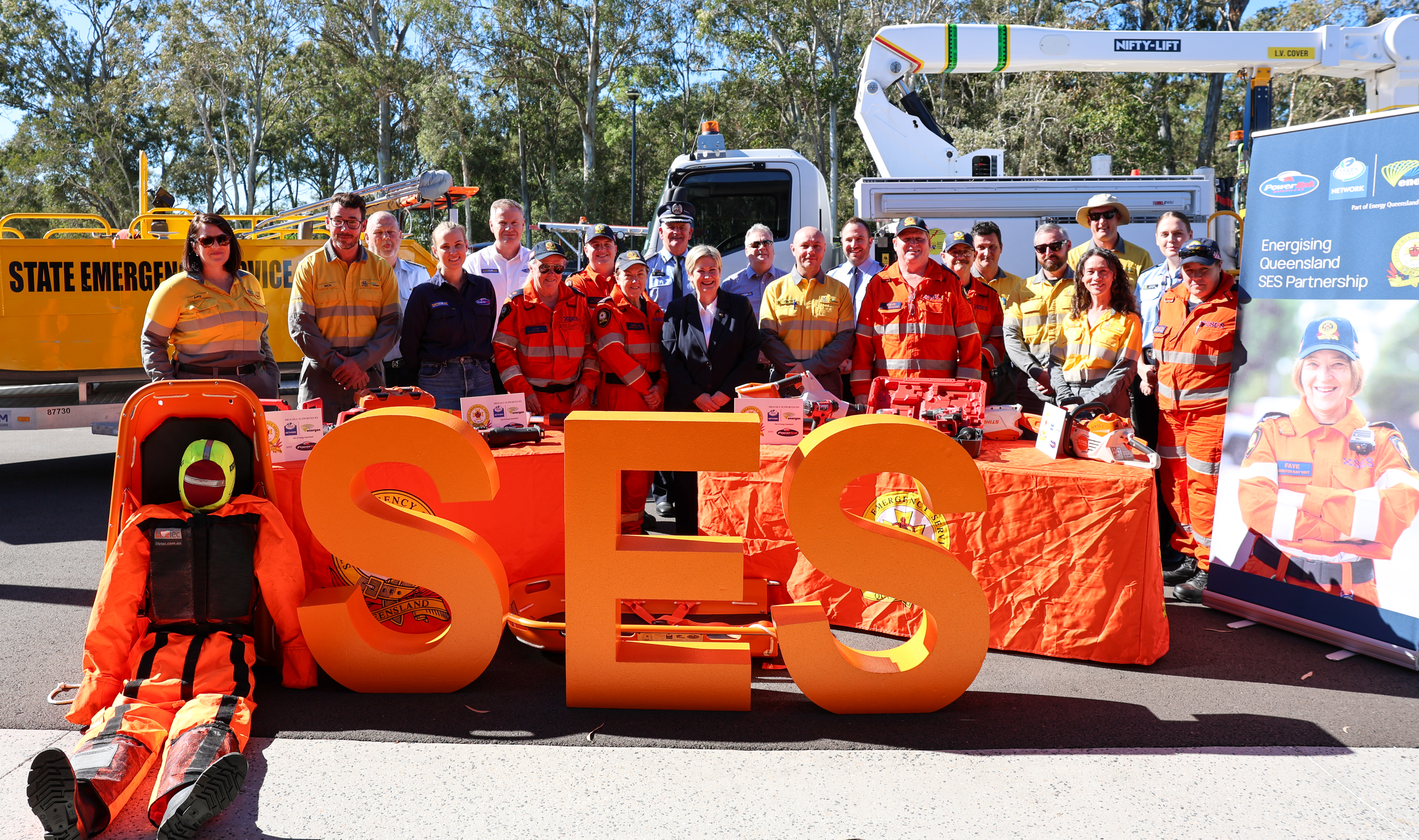 SES volunteers, Ergon and Powerlink standing in group photo behind emergency service equipment and large SES letters.