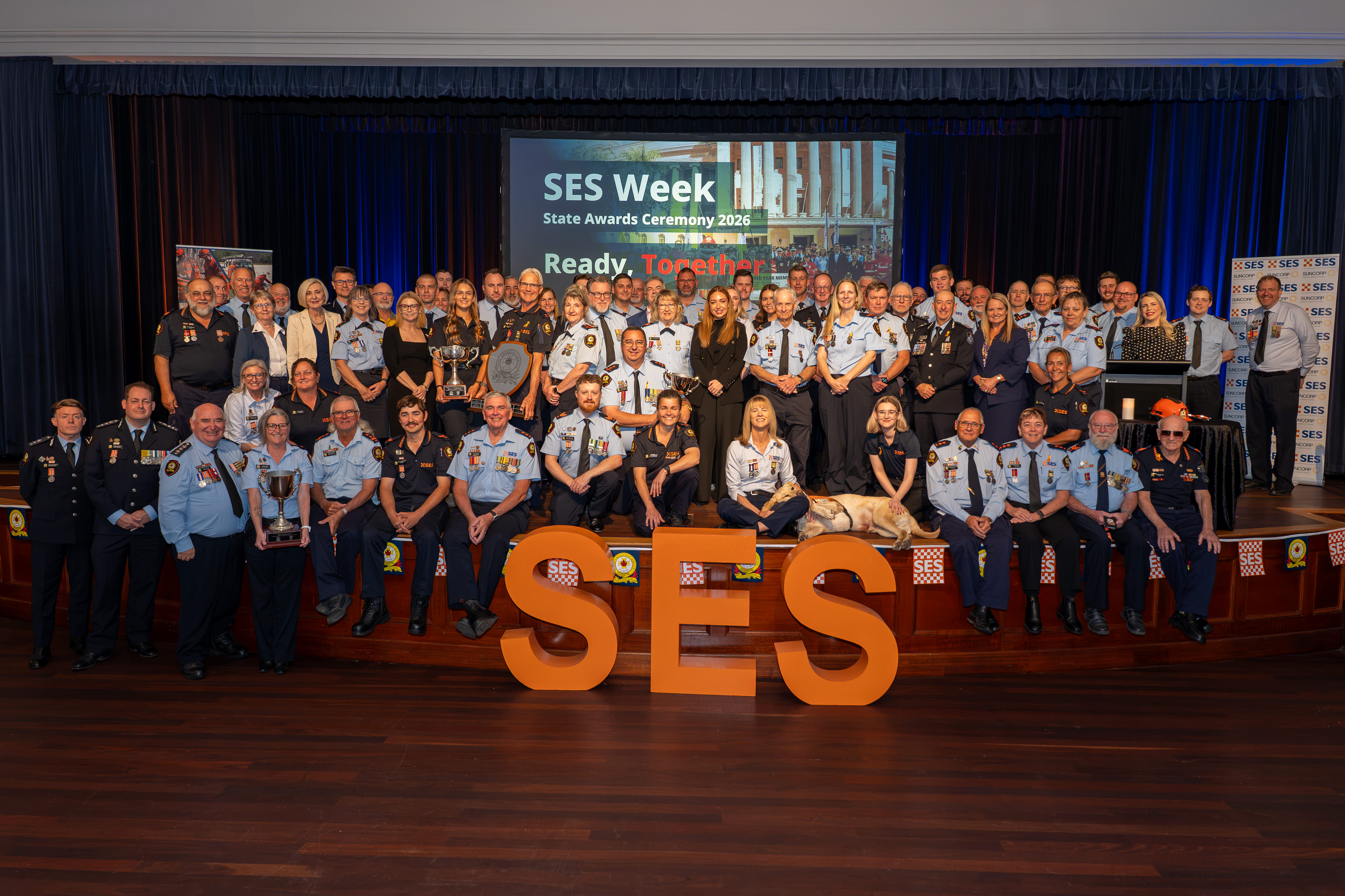 SES members and guests standing on stage in group arrangement with SES letters in front.