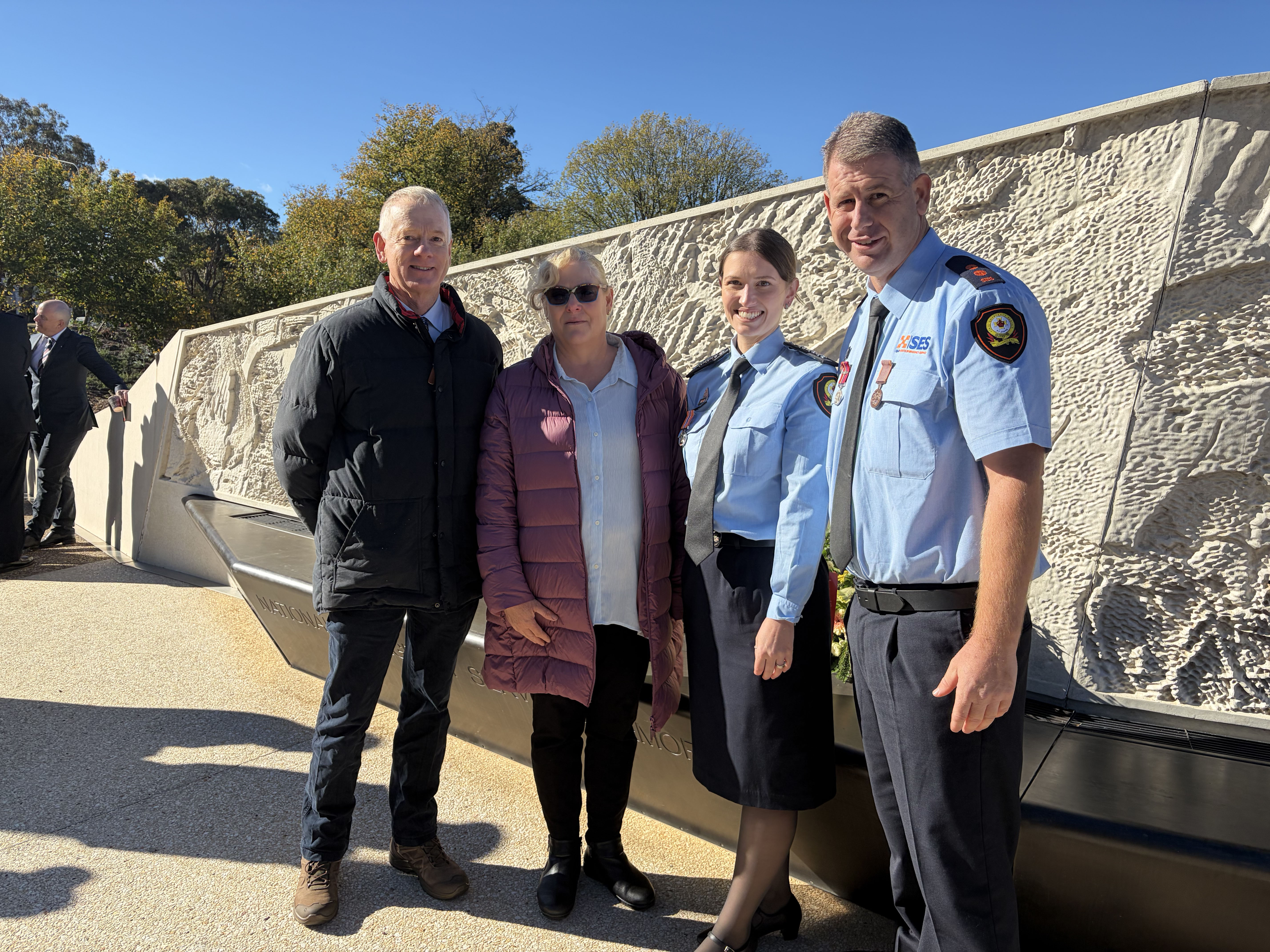 Rowen Taylor, Melody Taylor, Emily Higgins and Ben Reedman stand in front of a cream stone art section of the National Emergency Services Memorial.