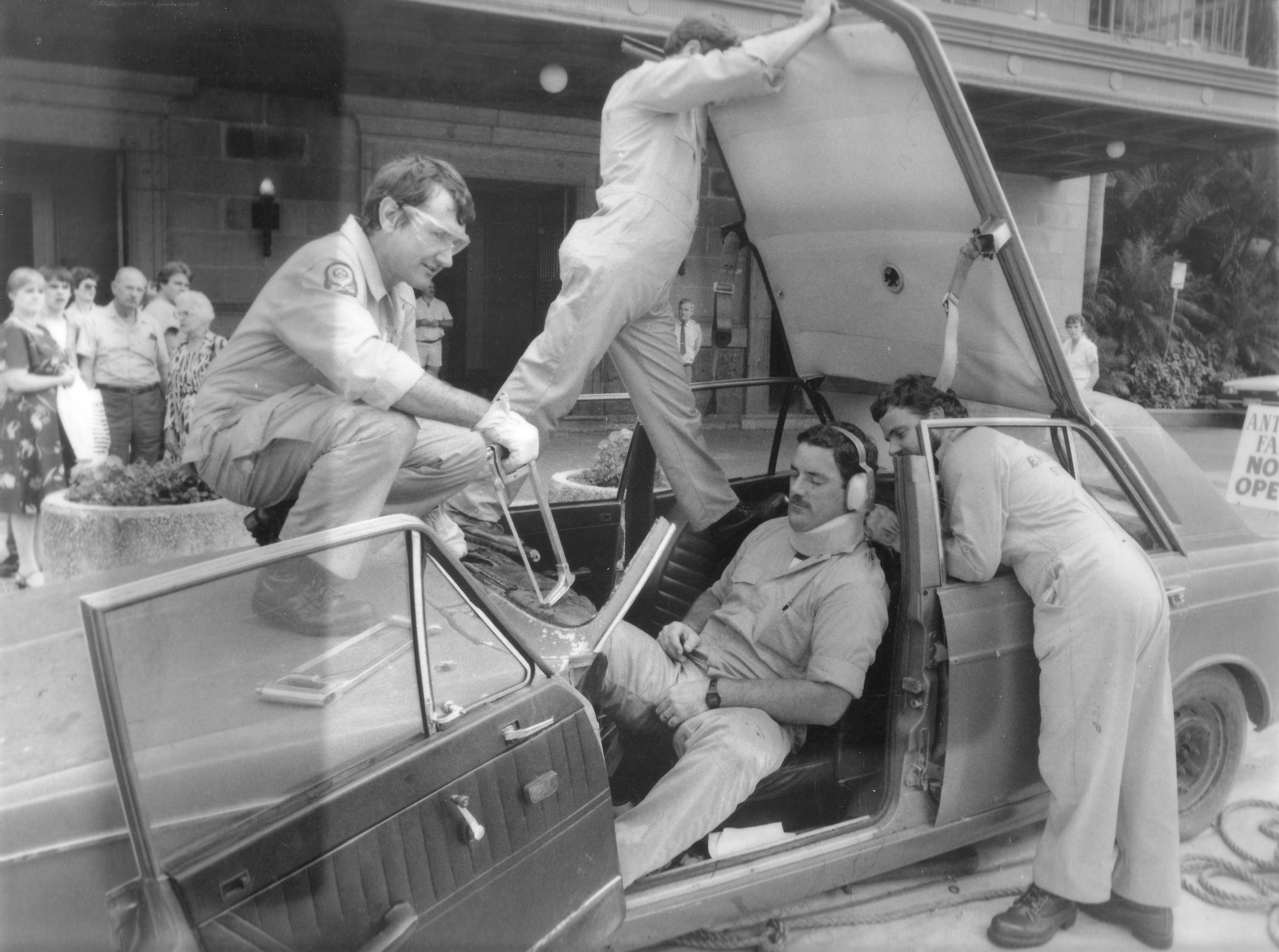 Black and white photo of three SES personnel removing a colleague from a simulated car crash